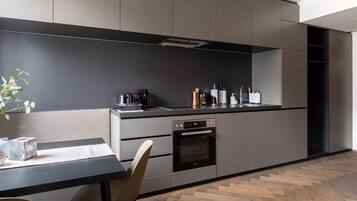 Una cocina moderna con salpicadero oscuro, electrodomésticos de acero inoxidable y suelo de madera en patrón de espiga.