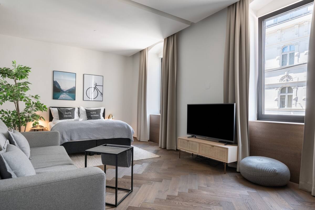 Ein modernes Hotelzimmer mit Bett, Sofa, Fernseher und einem großen Fenster mit Vorhängen.