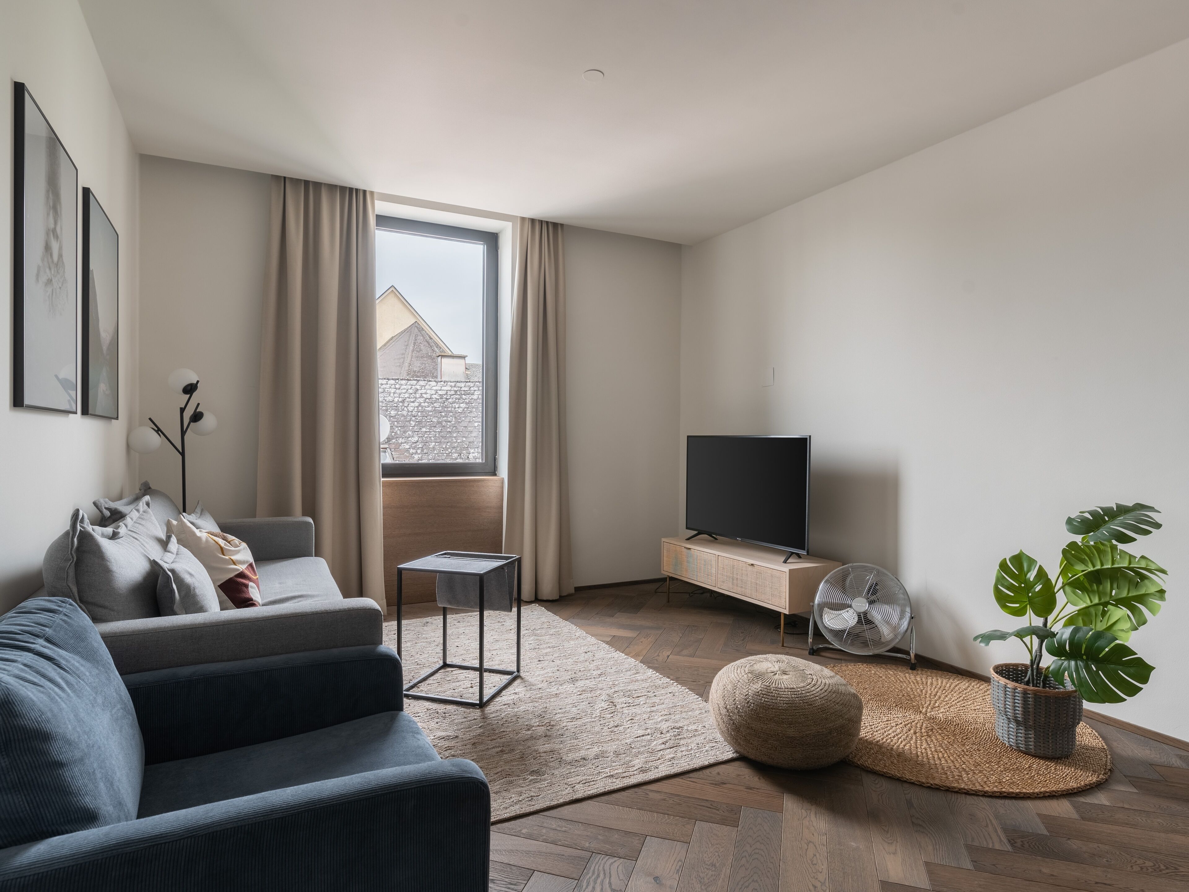 Een moderne woonkamer met een bank, een flatscreen televisie, een klein bijzettafeltje, een potplant en uitzicht buiten door een groot raam.