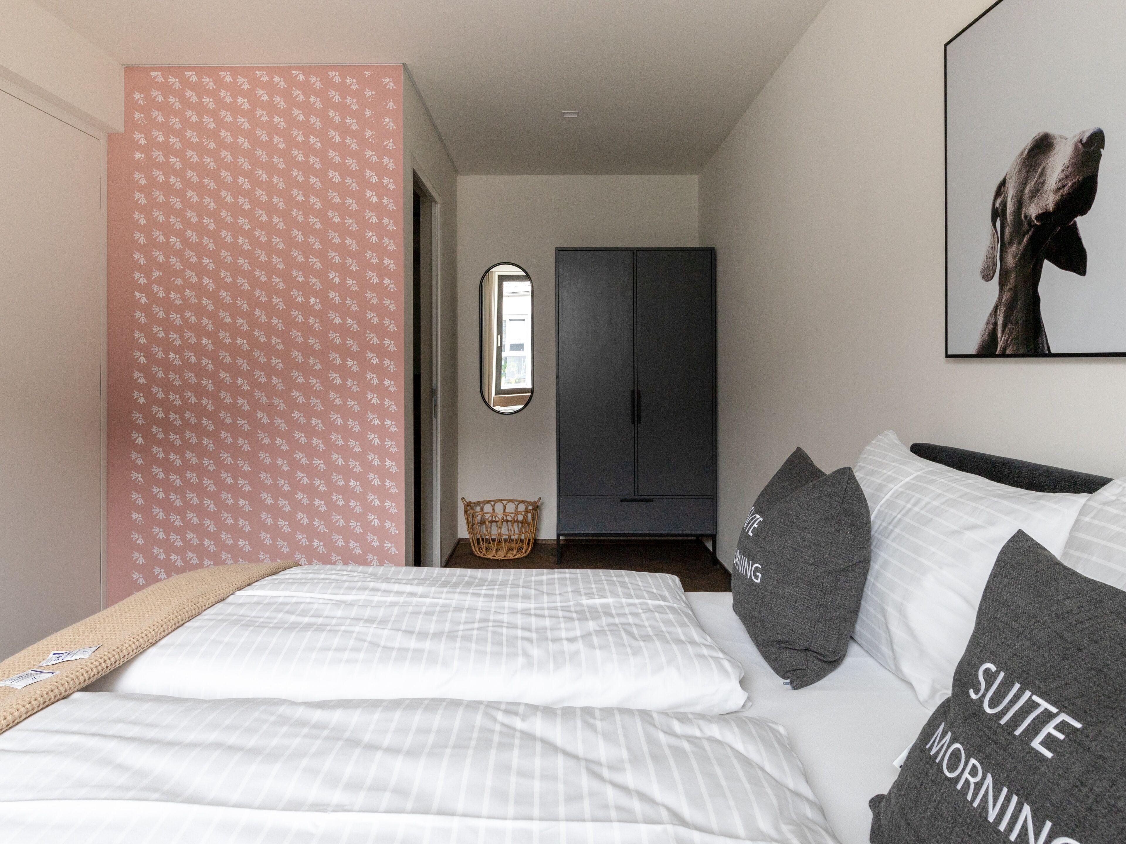 A modern bedroom with a bed, pillows, a wardrobe, and a mirror.