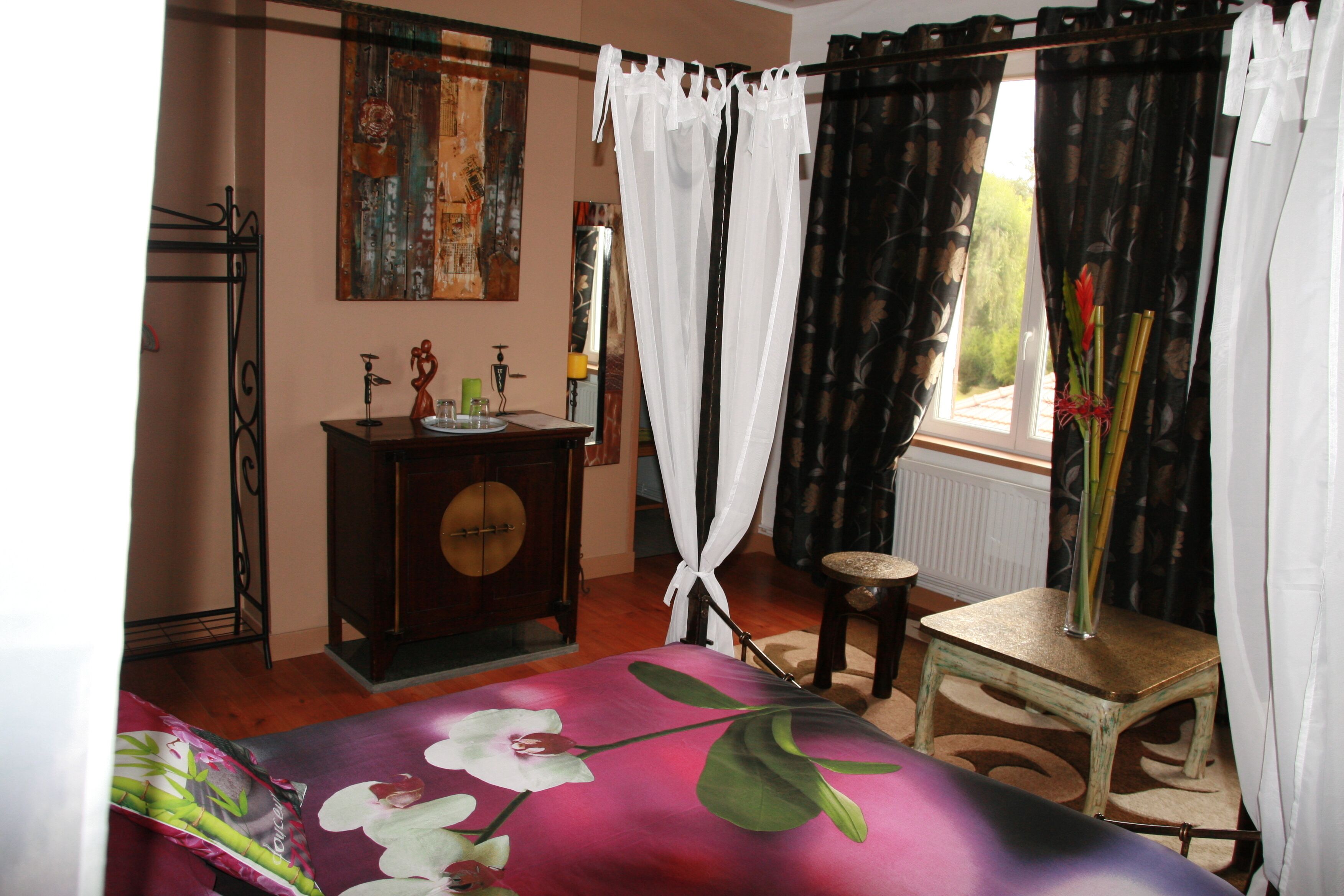 Un dormitorio con cama, cómoda, silla, ventana con cortinas y un cuadro en la pared.