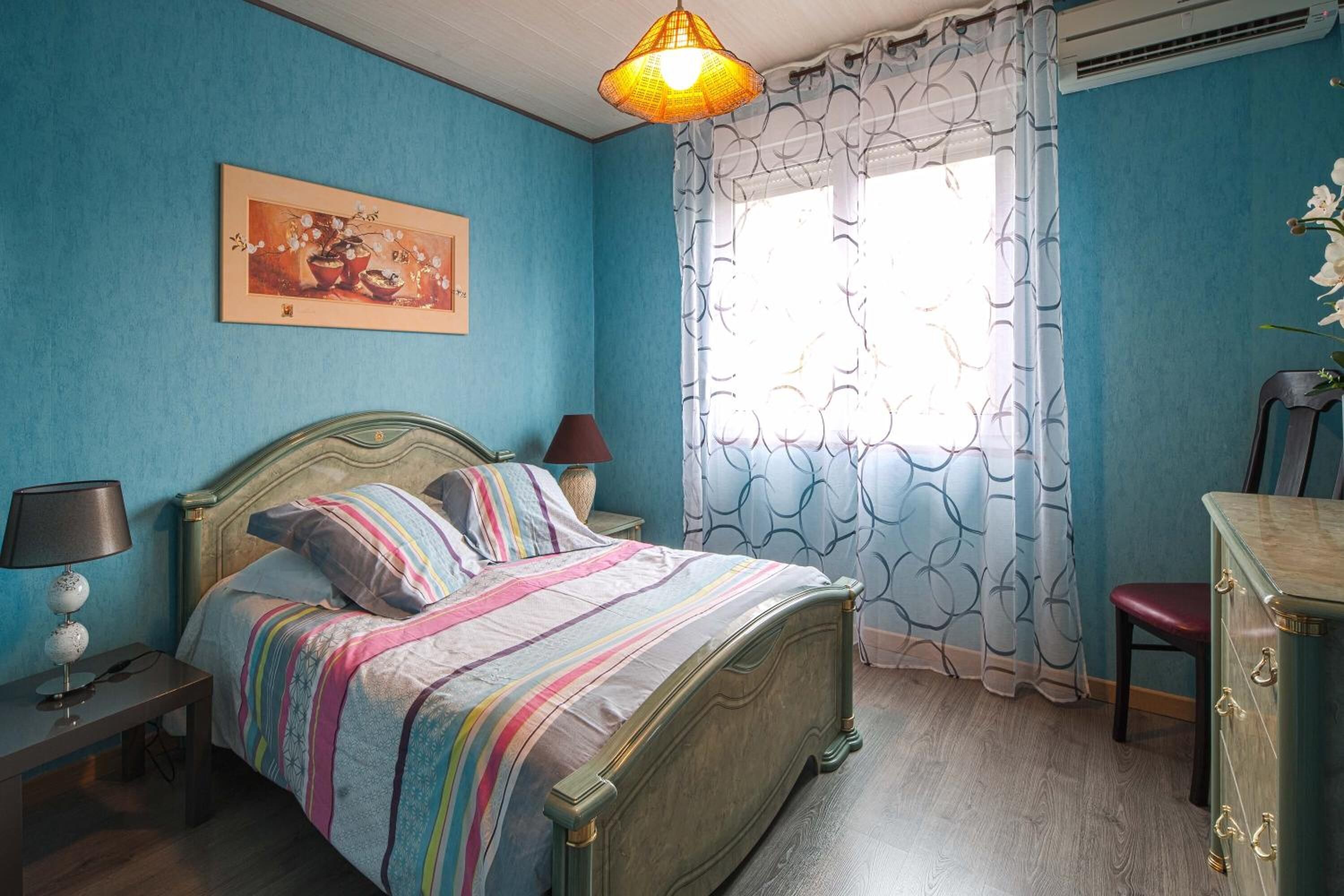 Una camera da letto con un letto, un comodino, una lampada, una cassettiera e una finestra con tende.