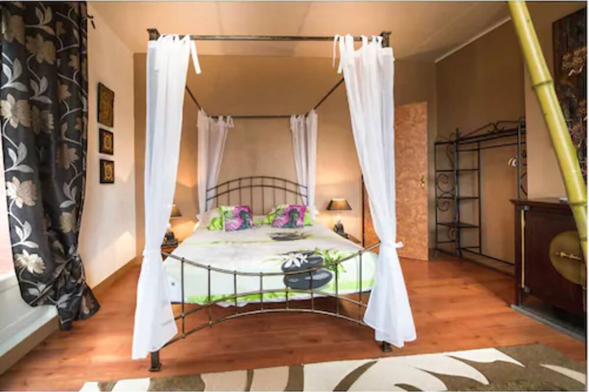 A four-poster canopy bed with a metal frame, white bedding, and decorative pillows.