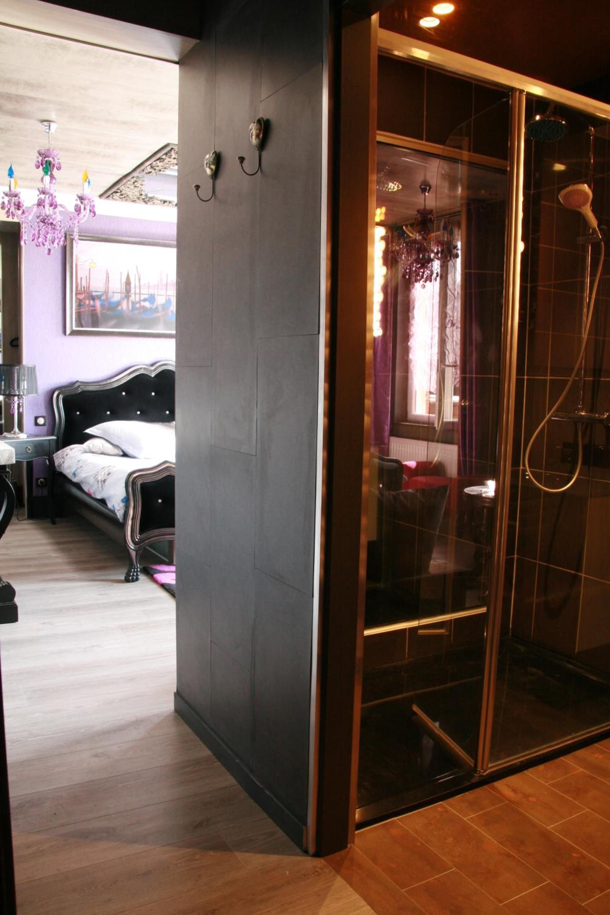 Un baño moderno con cabina de ducha de vidrio, una cama con cabecera negra y suelo de madera.