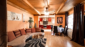 A cozy living room with a sofa, a coffee table, and a dining area with a table and chairs. - Chambres et Gites La Paysanne (Fresnes-en-Woevre)