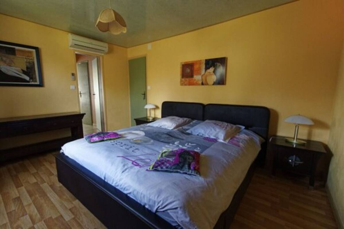 A bedroom with a bed, two bedside tables, a nightstand, a door, and a wall-mounted air conditioner.