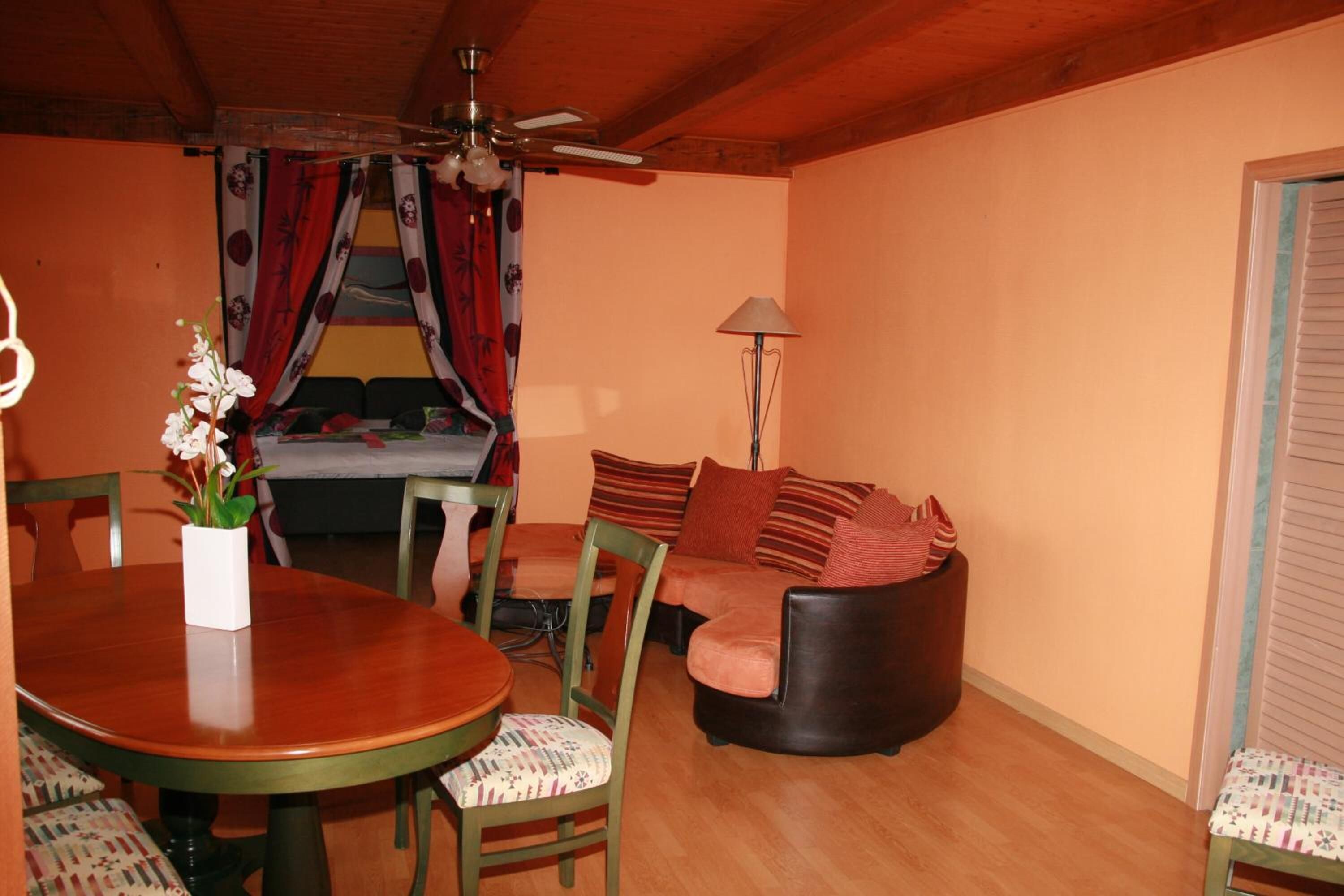 Une pièce chaleureuse avec une table à manger en bois, des chaises, un canapé et un ventilateur de plafond.