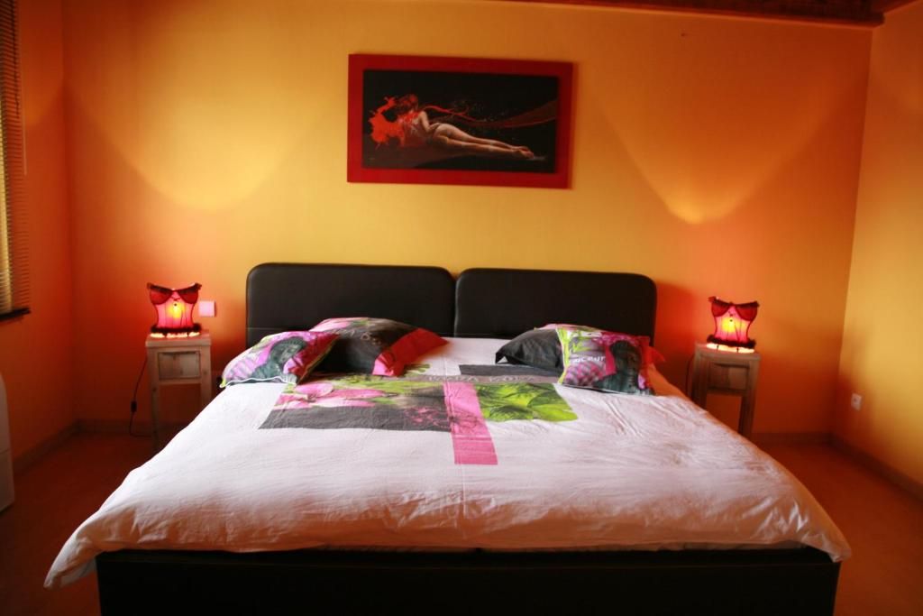 Una cama con edredón blanco y varias almohadas, dos lámparas de noche y un cuadro en la pared.