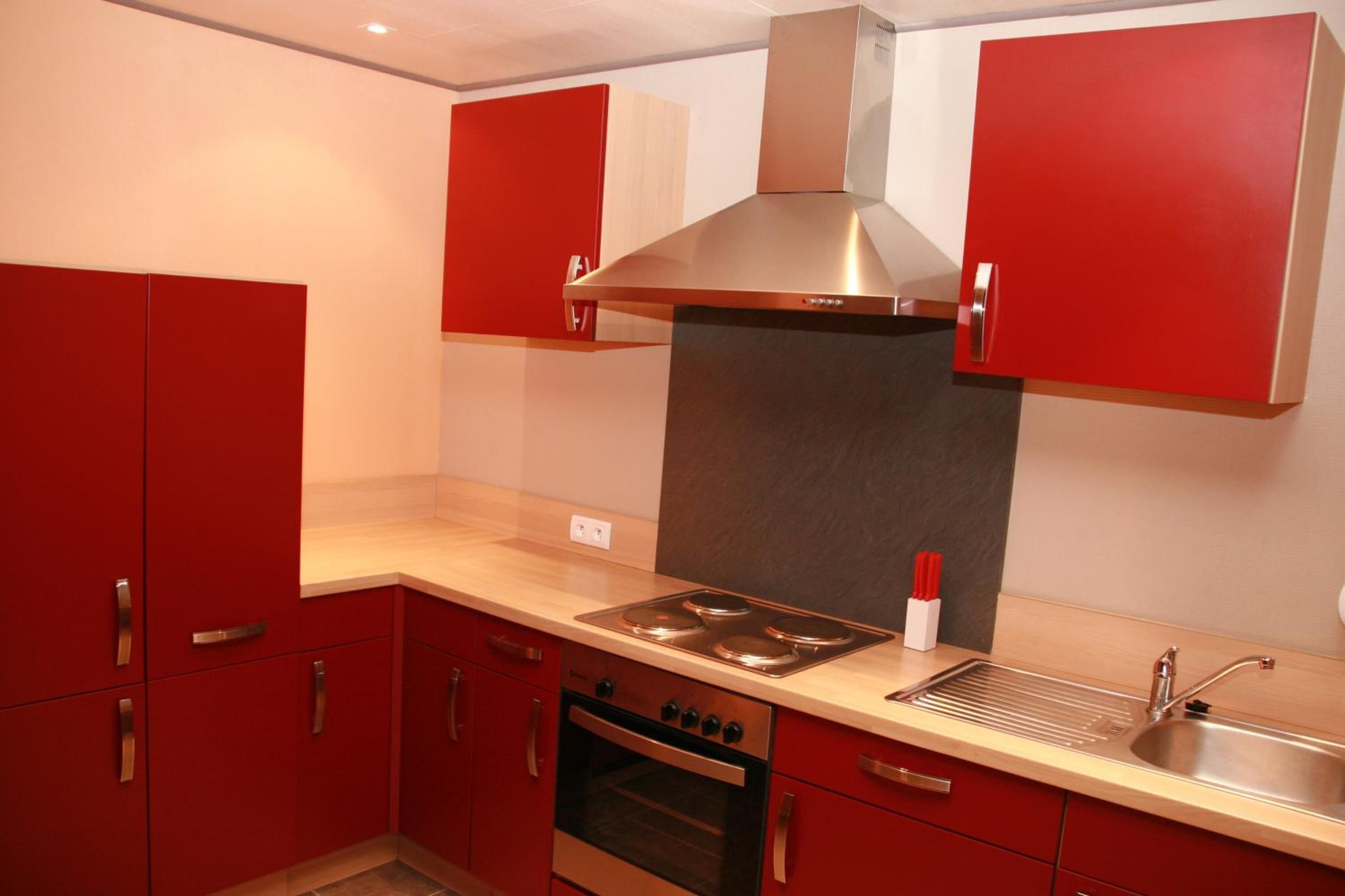 A modern kitchen with red cabinets, stainless steel appliances, and a built-in oven.