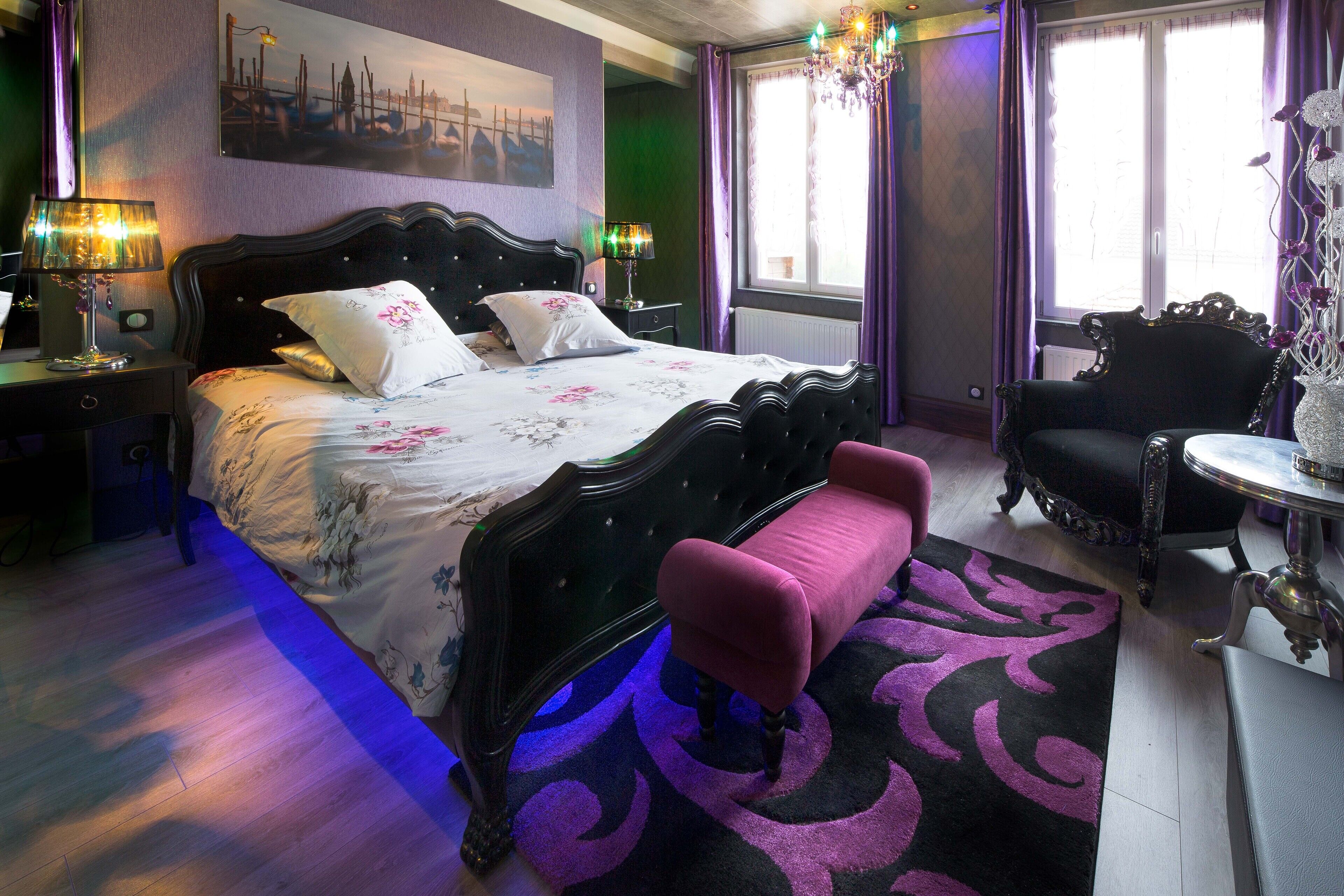 A bedroom with a large bed, a chair, a table, and a chandelier.