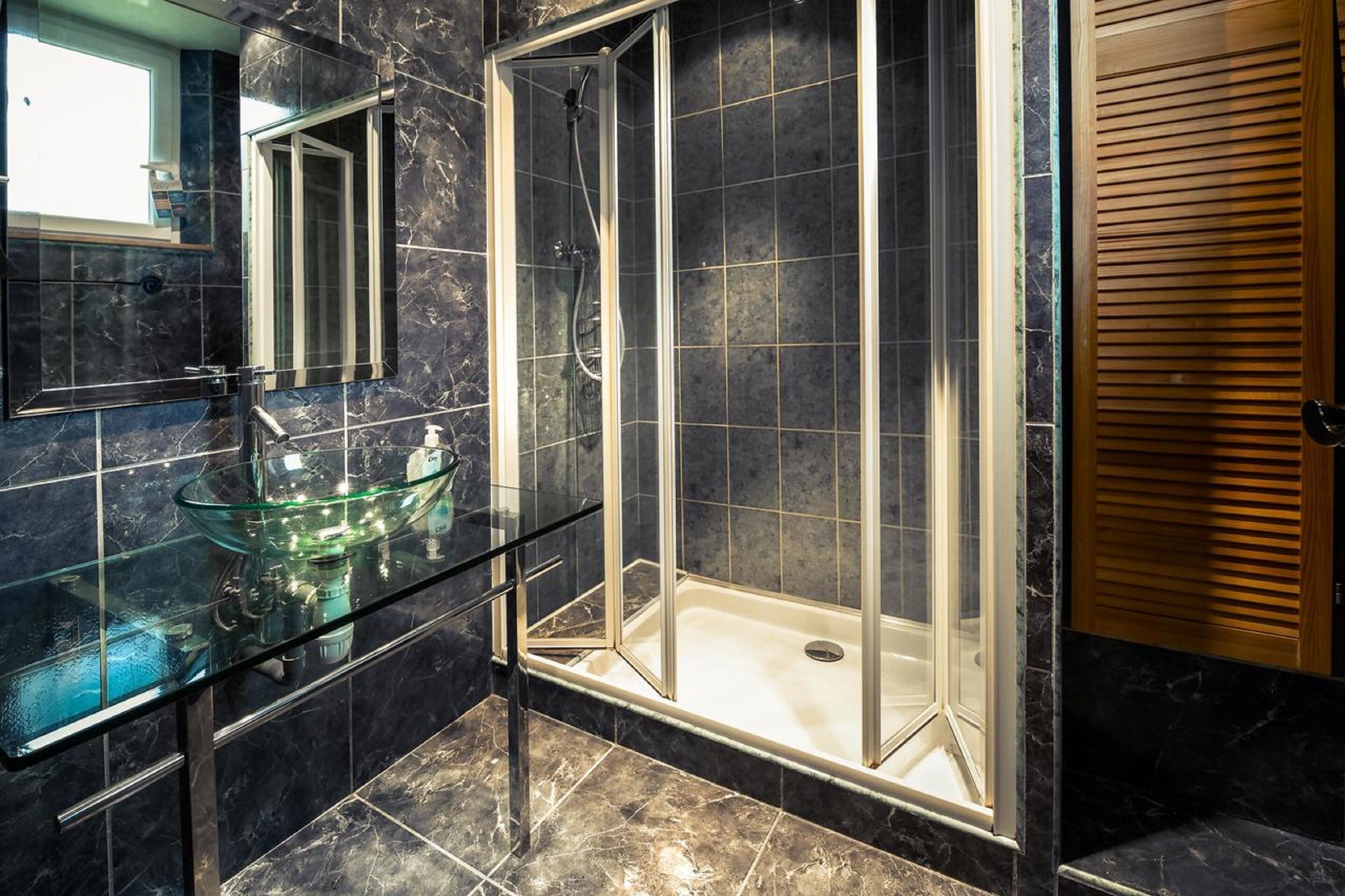 Ein modernes Badezimmer mit einem Waschbecken aus Glas, einer begehbaren Dusche und einer Holztür.