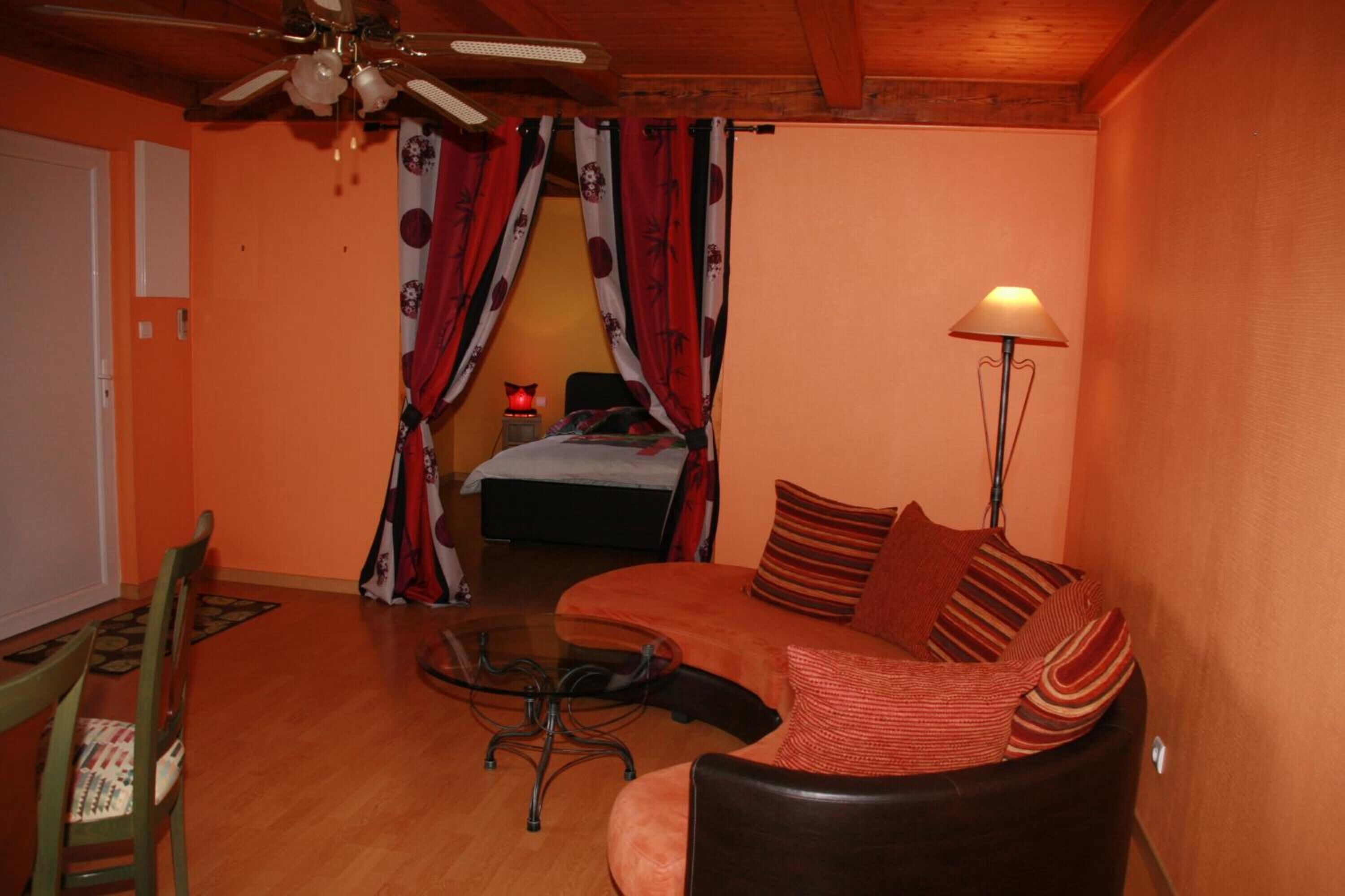 Une pièce chaleureuse avec un plafond en bois, un lit doté de rideaux rouges et blancs, un canapé agrémenté de coussins à rayures et un lampadaire.