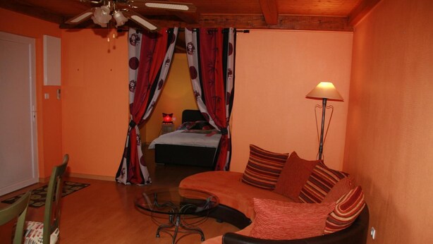 Una habitación acogedora con techo de madera, cama con cortinas rojas y blancas, sofá con cojines a rayas y una lámpara de pie.