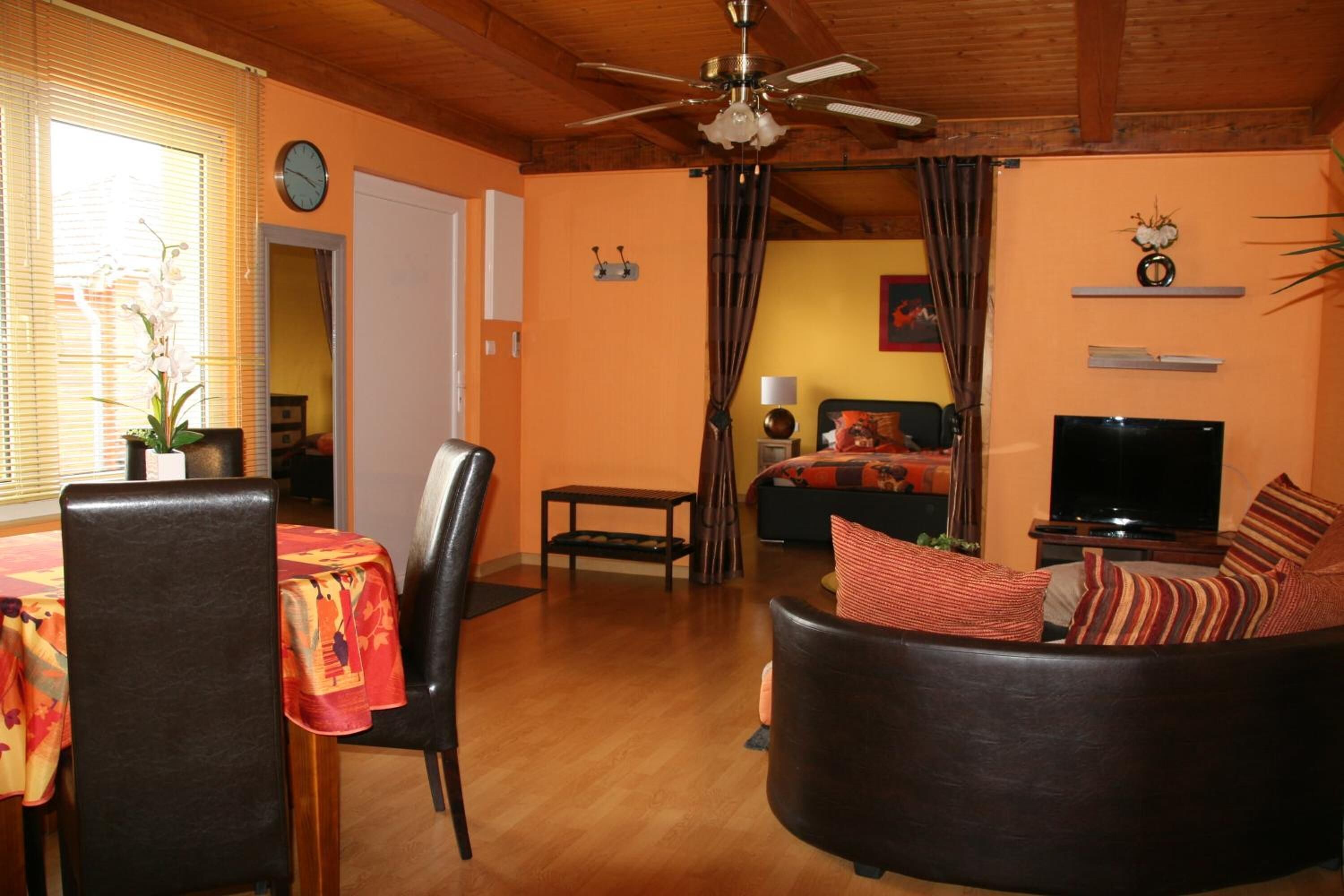 A living room with a ceiling fan, a sofa with striped cushions, a dining table with chairs, and a television.