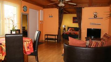 A living room with a ceiling fan, a sofa with striped cushions, a dining table with chairs, and a television.