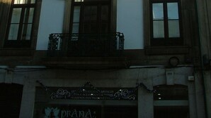 Un immeuble à plusieurs étages, doté d’une façade blanche, de nombreuses fenêtres à encadrements sombres et d’un balcon orné de rampes en métal ouvragé.
