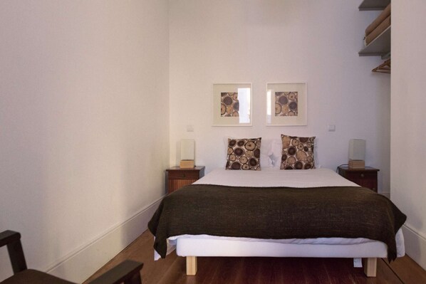 A bedroom with a bed, two bedside tables, and two wall-mounted lamps. - One-Bedroom Apartment (Porto)
