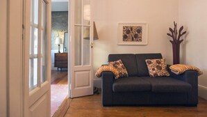 Une pièce avec un canapé gris foncé, deux coussins décoratifs à motifs, un tableau encadré au mur et un grand vase en bois.