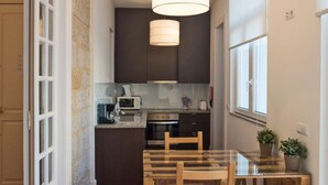 Une cuisine de taille réduite, dotée de meubles de rangement aux couleurs sombres, d’une table à manger en bois et d’un luminaire suspendu.