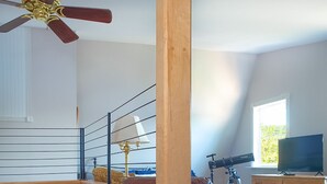 A multi-level living space with a staircase, a wooden table, a leather sofa, a television, and a telescope.