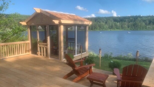 A wooden deck with a gazebo, chairs, and a table overlooking a lake.