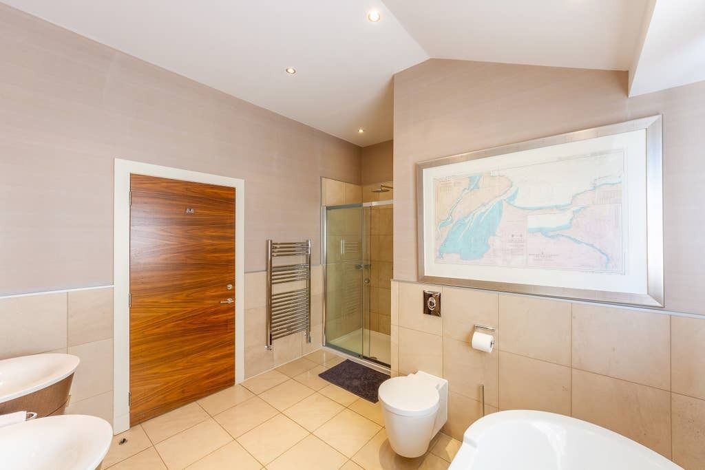 Een moderne badkamer met een houten deur, een douchecabine van glas, een wit toilet en een bad.