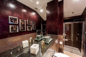 A modern bathroom with a dark marble wall, a glass shower enclosure, and a large mirror.