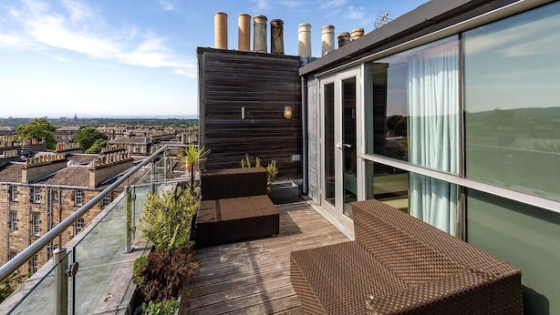 Eine Dachterrasse mit Holzboden, Sitzgelegenheiten im Freien und Blick auf die Stadt.