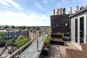A rooftop terrace with a view of the city, a modern building with large windows, and a metal railing.