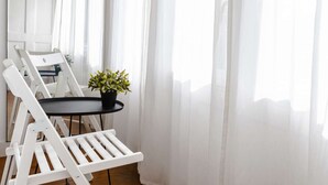 A white chair and table set against a window with sheer curtains.