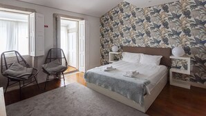 A bedroom with a bed, two nightstands, a chair, a rug, and a floral wallpaper.