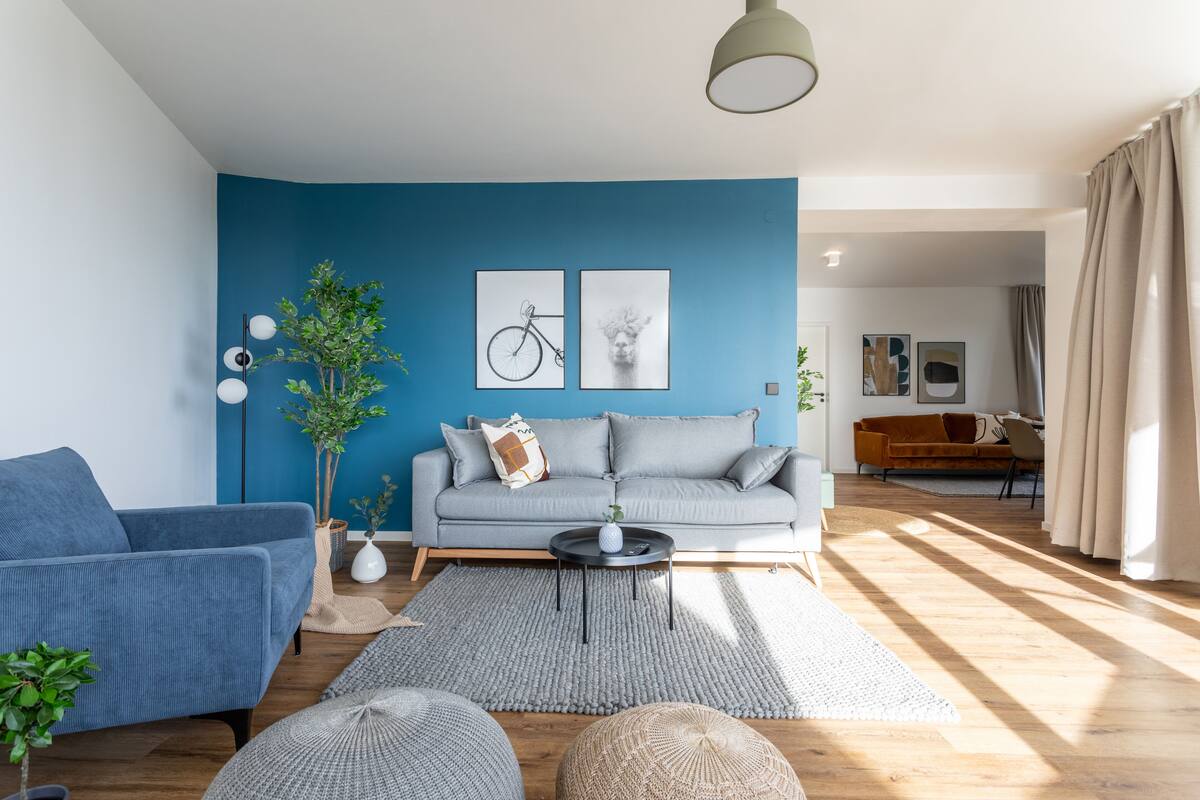 Ein modernes Wohnzimmer mit blauer Akzentwand, einem grauen Sofa, einem blauen Sessel und Holzboden.