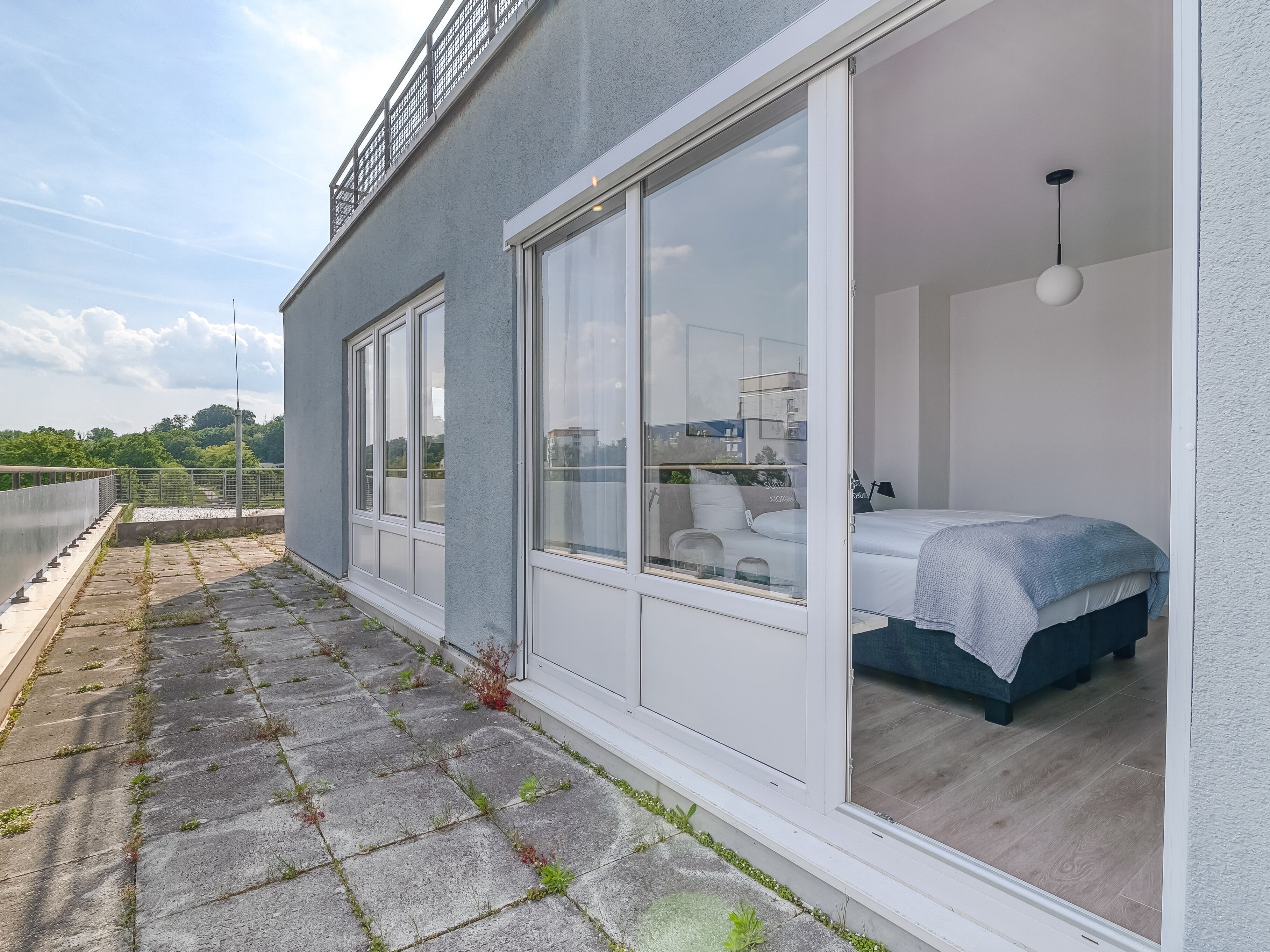 A modern bedroom with a large sliding glass door, a bed with a blue cover, and a white ceiling light.