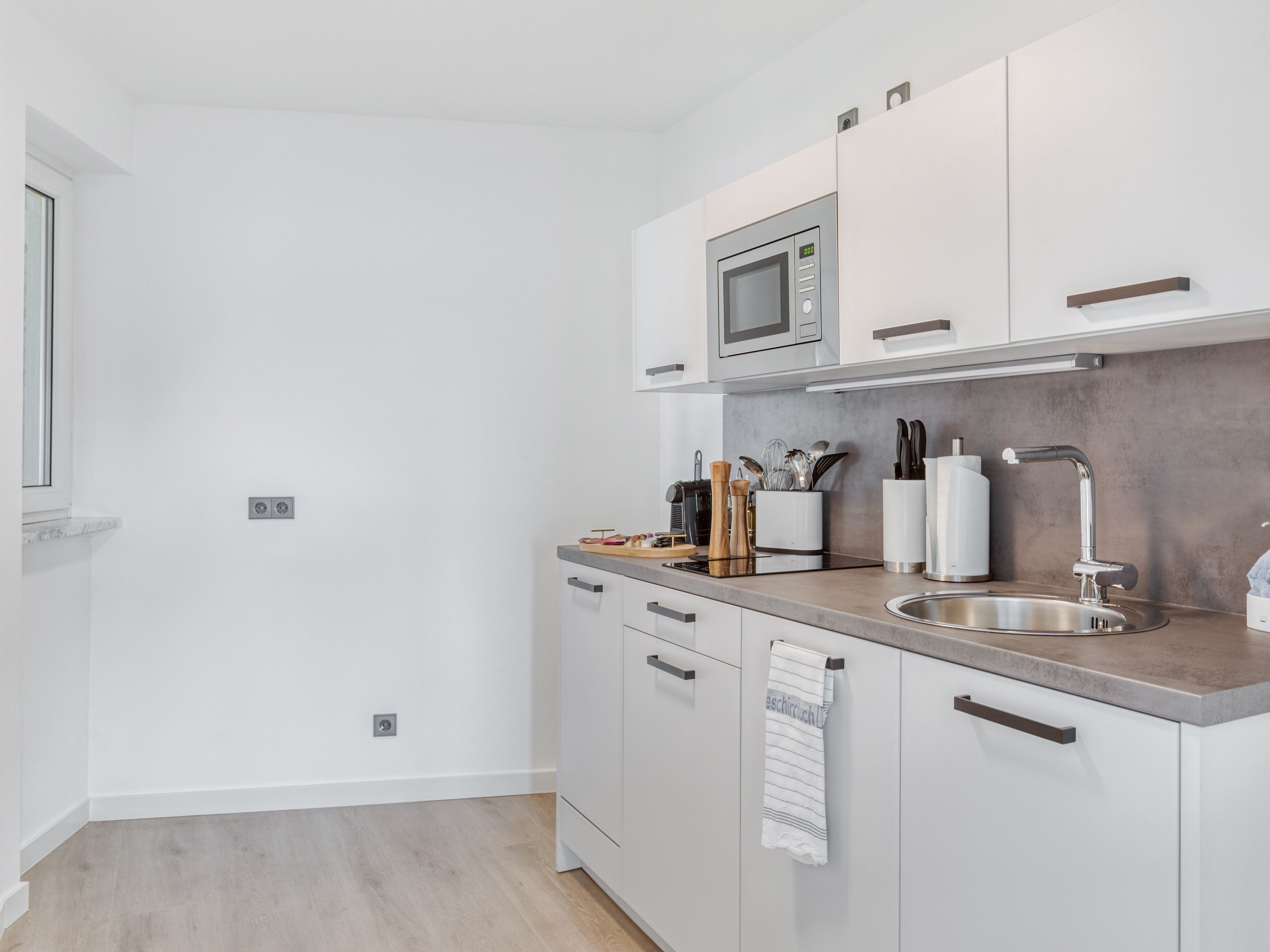 A modern kitchen with white cabinets, a stainless steel sink, and a microwave.