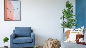Una sala moderna con un sillón azul, un sofá gris, una pequeña planta en maceta, una cesta de mimbre y un cuadro en la pared.