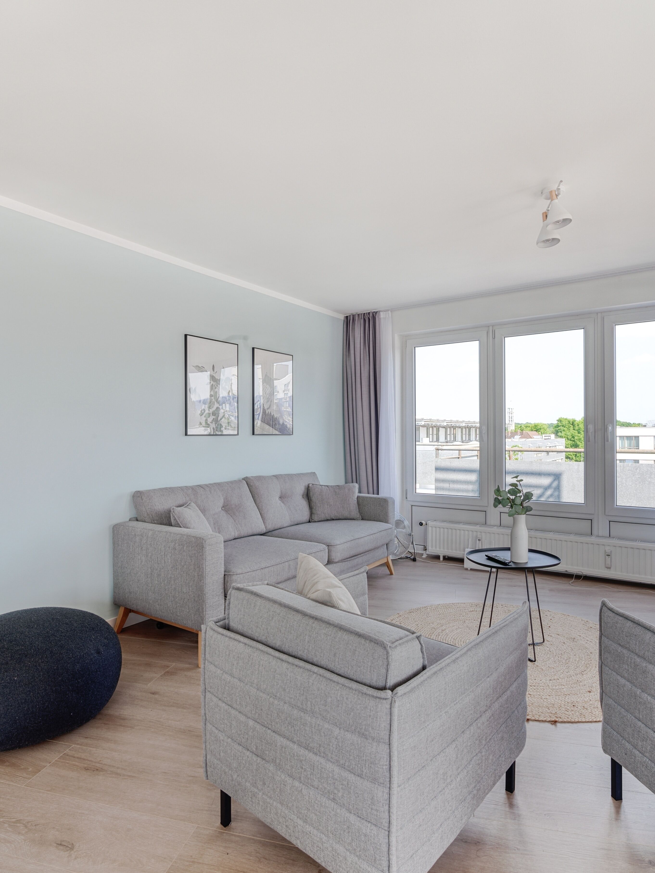 Una sala de estar moderna con un sofá seccional gris, un otoman redondo y una pequeña mesa redonda con un jarrón.