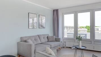 Una sala de estar moderna con un sofá seccional gris, un otoman redondo y una pequeña mesa redonda con un jarrón.