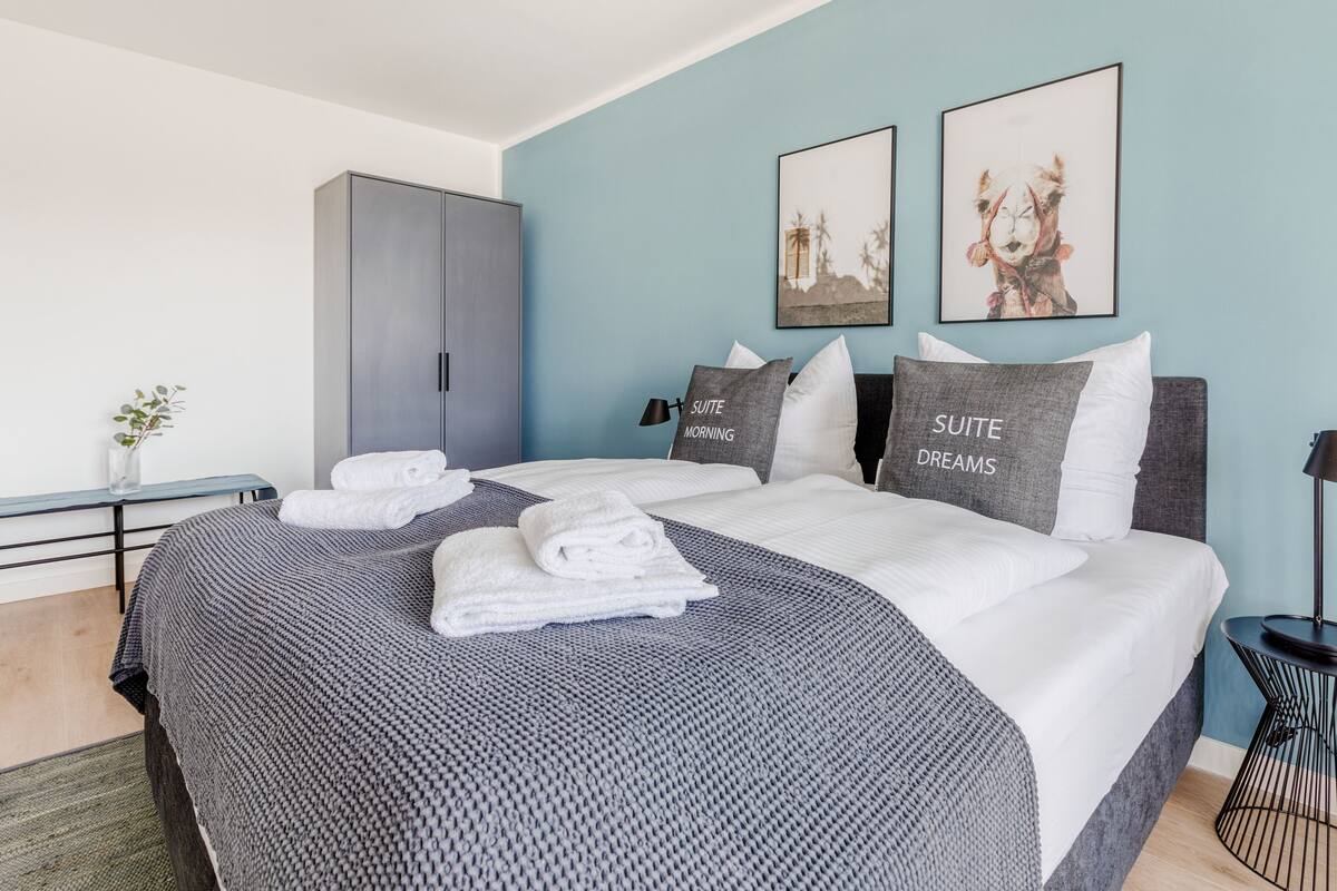 Ein modernes Schlafzimmer mit einem Bett, zwei Kissen, einem Nachttisch, einem Kleiderschrank und zwei gerahmten Bildern an der Wand.