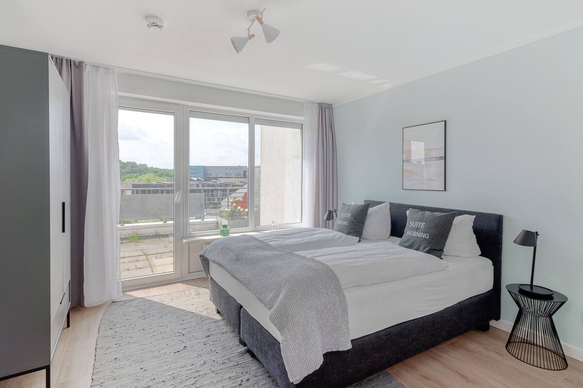 Ein modernes Schlafzimmer mit einem großen Bett, einem Nachttisch und Blick ins Freie.