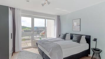 A modern bedroom with a large bed, a side table, and a view of the outdoors.