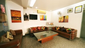 A modern hotel lobby with a brown leather sofa set, a glass-top coffee table, and various artworks on the walls. - ADB Rooms Hotel Noratan Palace (New Delhi)