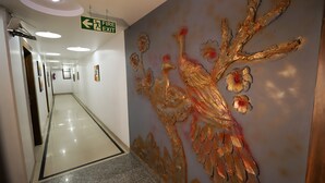 A hallway with a polished floor, a fire exit sign, and a wall with a golden abstract design. - ADB Rooms Hotel Noratan Palace (New Delhi)