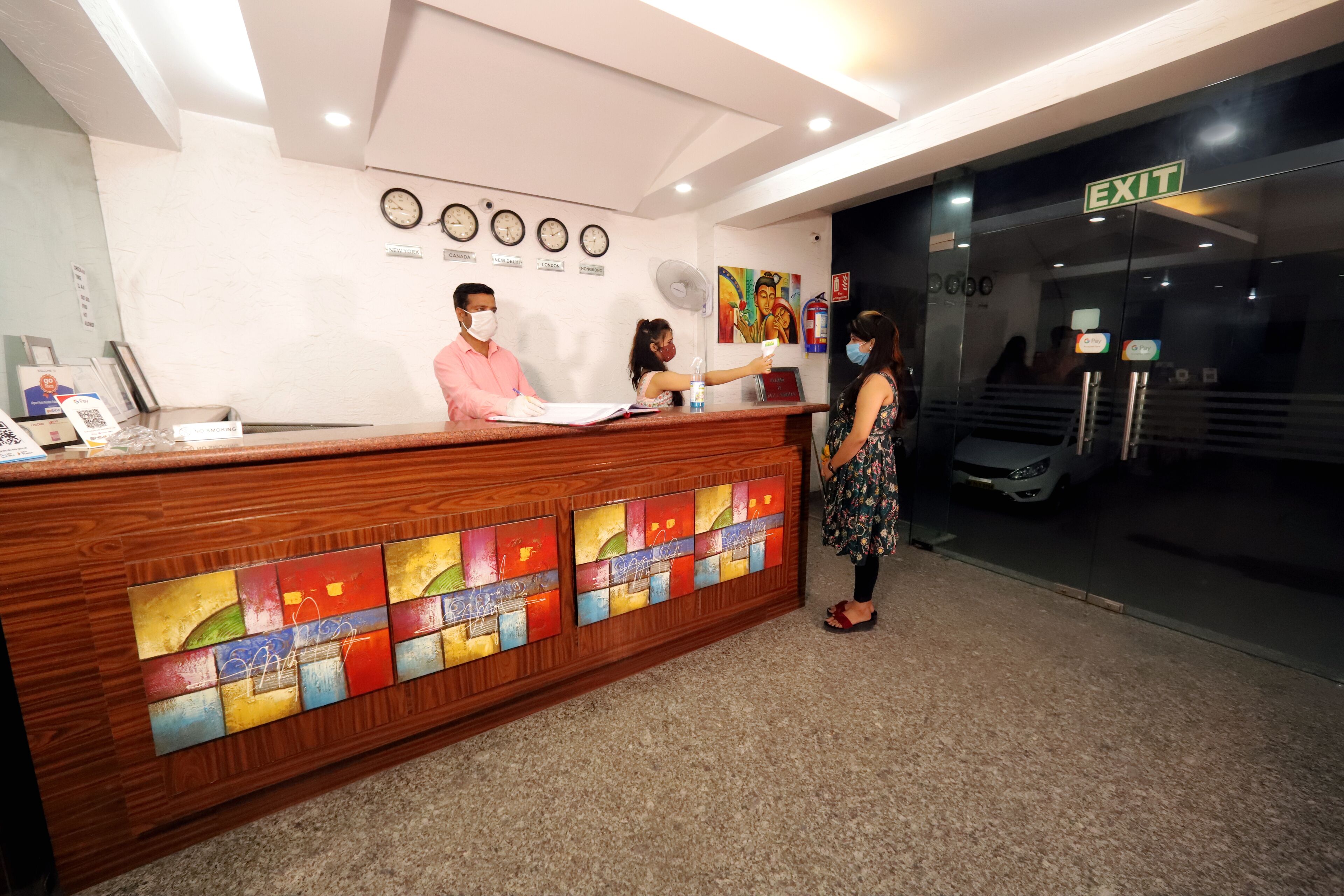 A reception desk with a wooden finish and colorful stained glass panels. There are clocks on the wall and an exit sign above the door.
