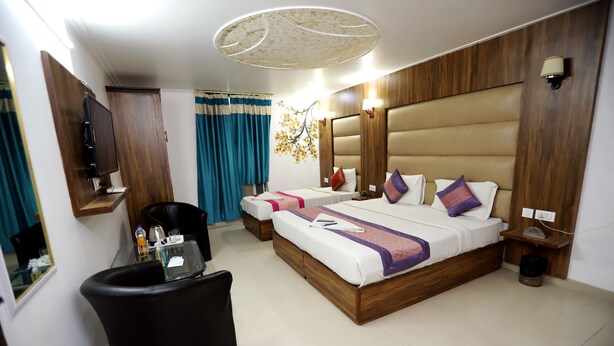A hotel room with a large bed, a desk with a chair, a TV, and a ceiling light fixture. - ADB Rooms Hotel Noratan Palace (New Delhi)