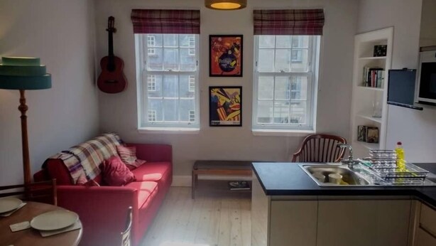 En kompakt bolig med tekøkken, en rød sofa, en guitar og kunst på væggene.