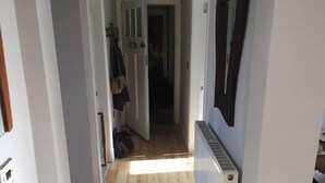 En smal gang med trægulv, hvide vægge og en radiator til højre.