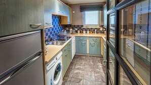 A compact kitchen with a washing machine, a sink, and a window with blinds. - Contemporary Holyrood Apartment (Edinburgh)