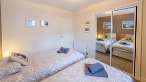 A hotel room with two beds, a large mirror, and a door leading to another room. - Contemporary Holyrood Apartment (Edinburgh)