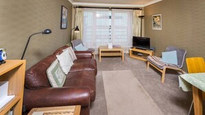 A living room with a brown leather sofa, a wooden coffee table, a TV stand, a lamp, and a window with curtains. - Contemporary Holyrood Apartment (Edinburgh)