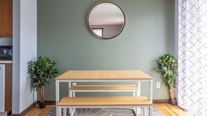 Una habitación con una mesa de madera y un banco, un espejo redondo en la pared y dos plantas en macetas.